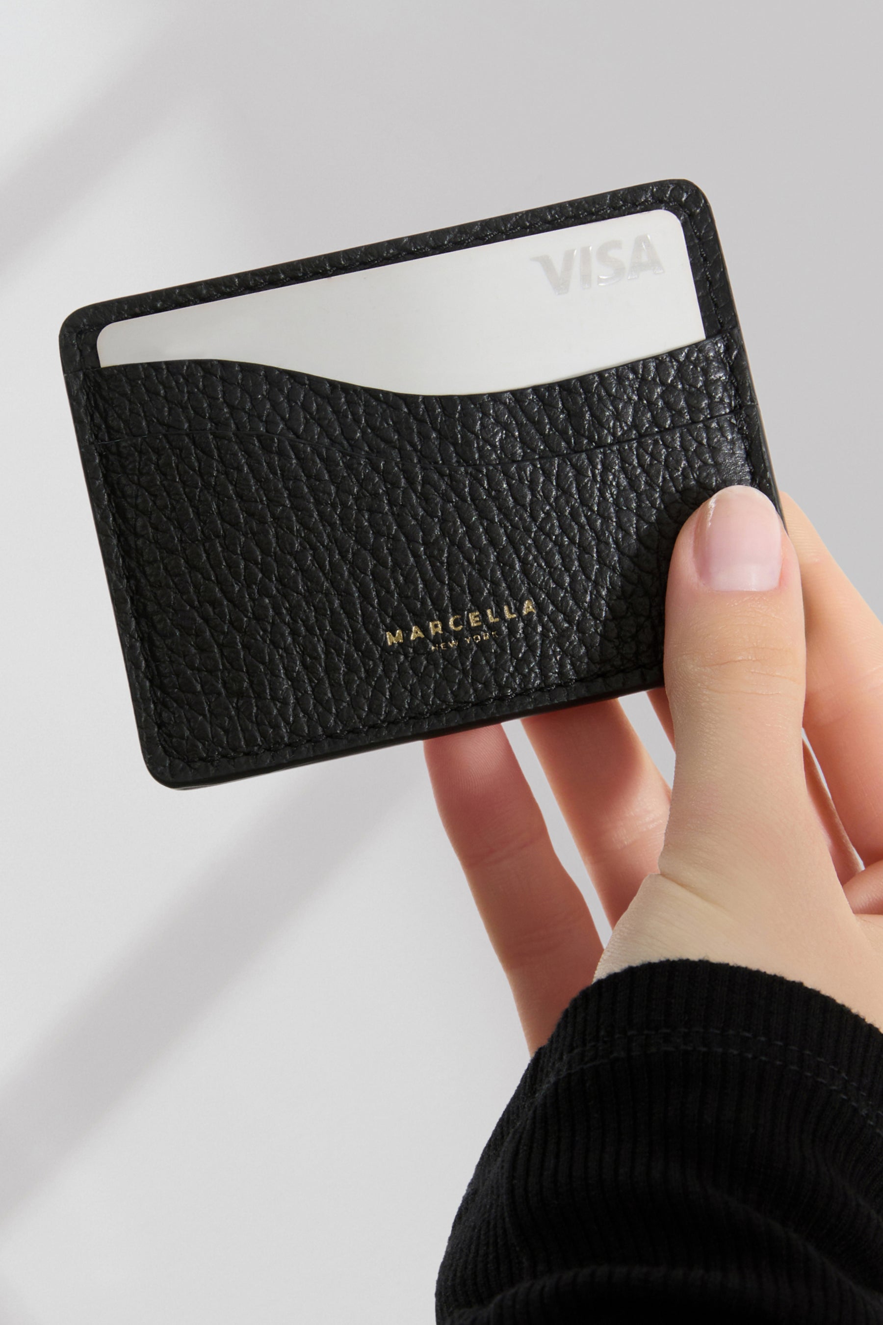 Black pebbled leather card holder with gold text, holding a white card visible at the top.