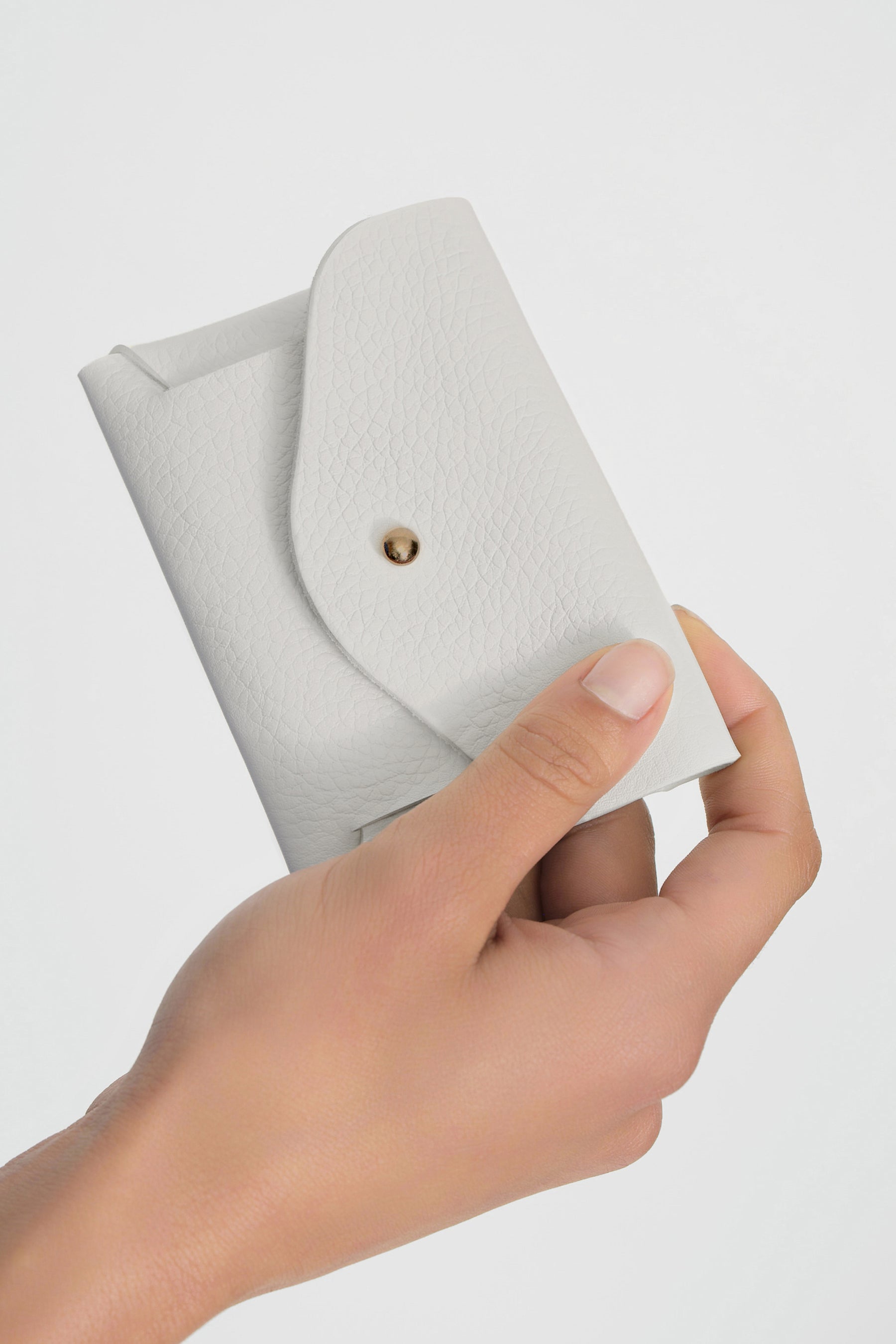 White quilted leather pouch with snap closure held in hand against neutral background.