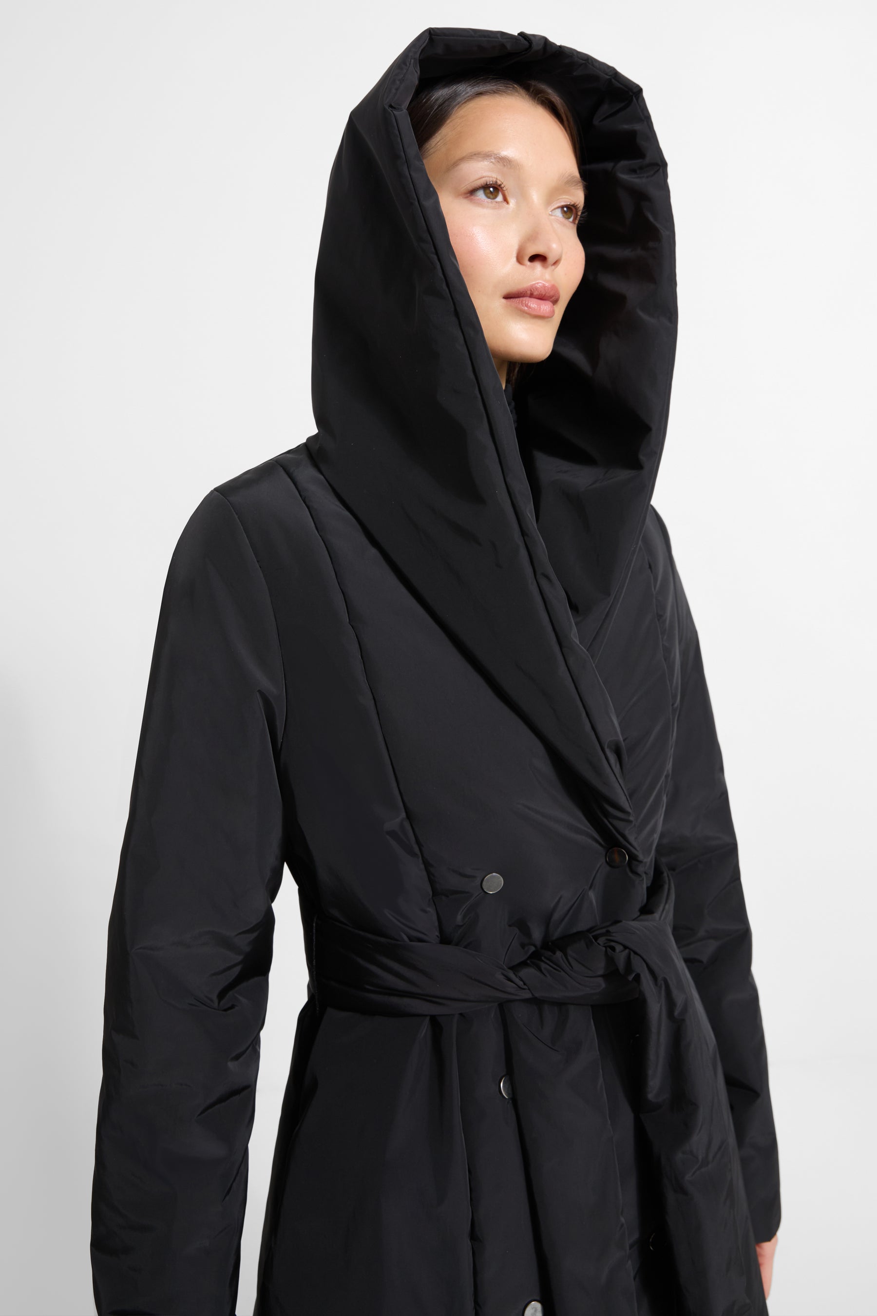 Black hooded puffer jacket with drawstring waist and button closure, worn with hood up.