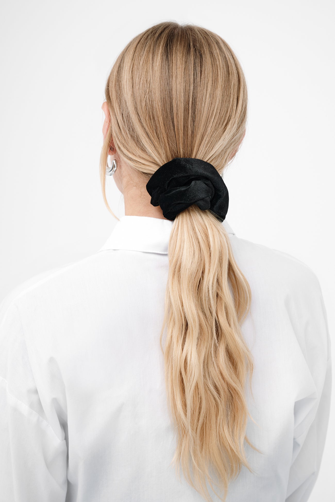 Black velvet scrunchie holding a blonde ponytail on the back of a person's head.