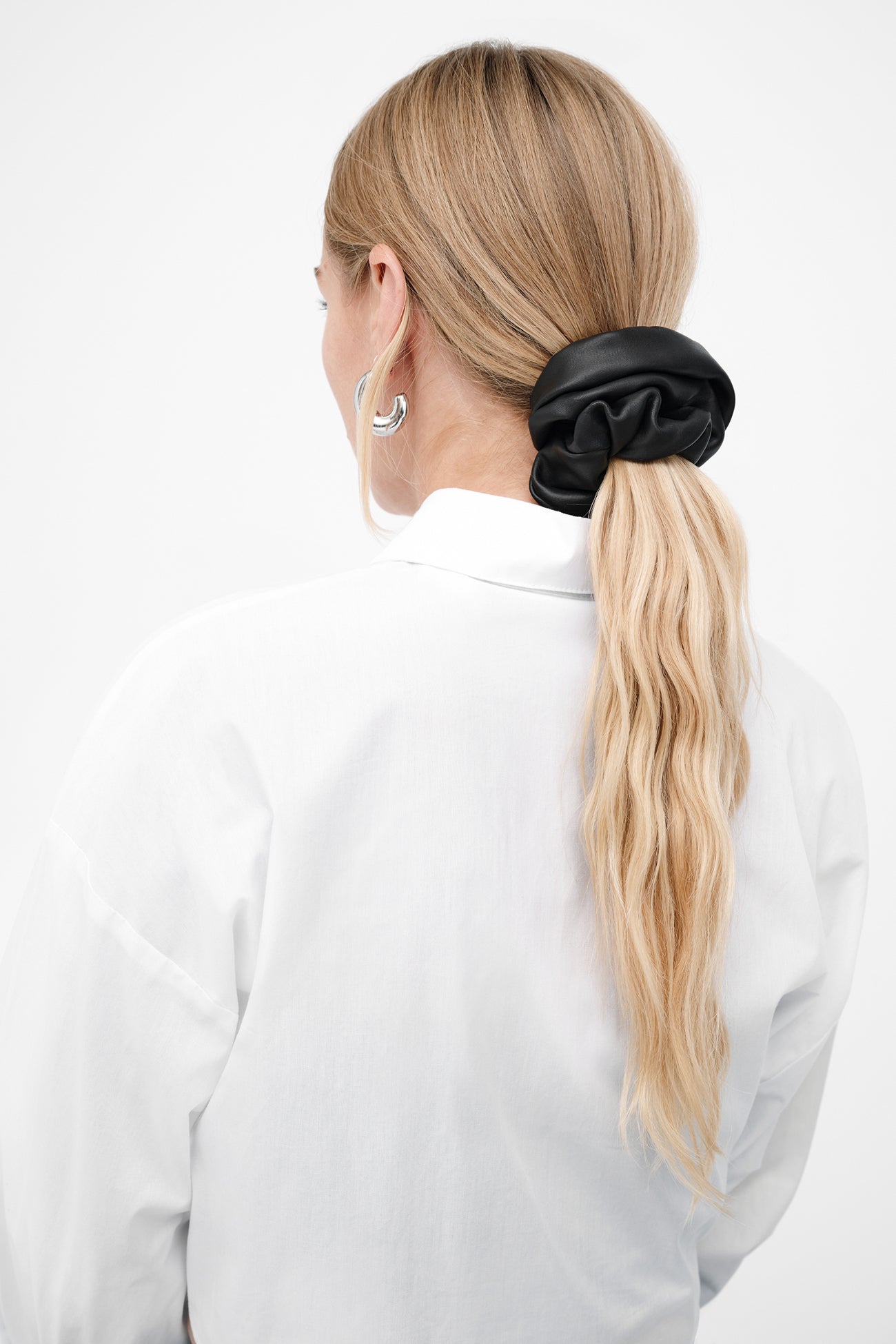 Black satin scrunchie holding blonde hair in a ponytail, worn on person from behind.