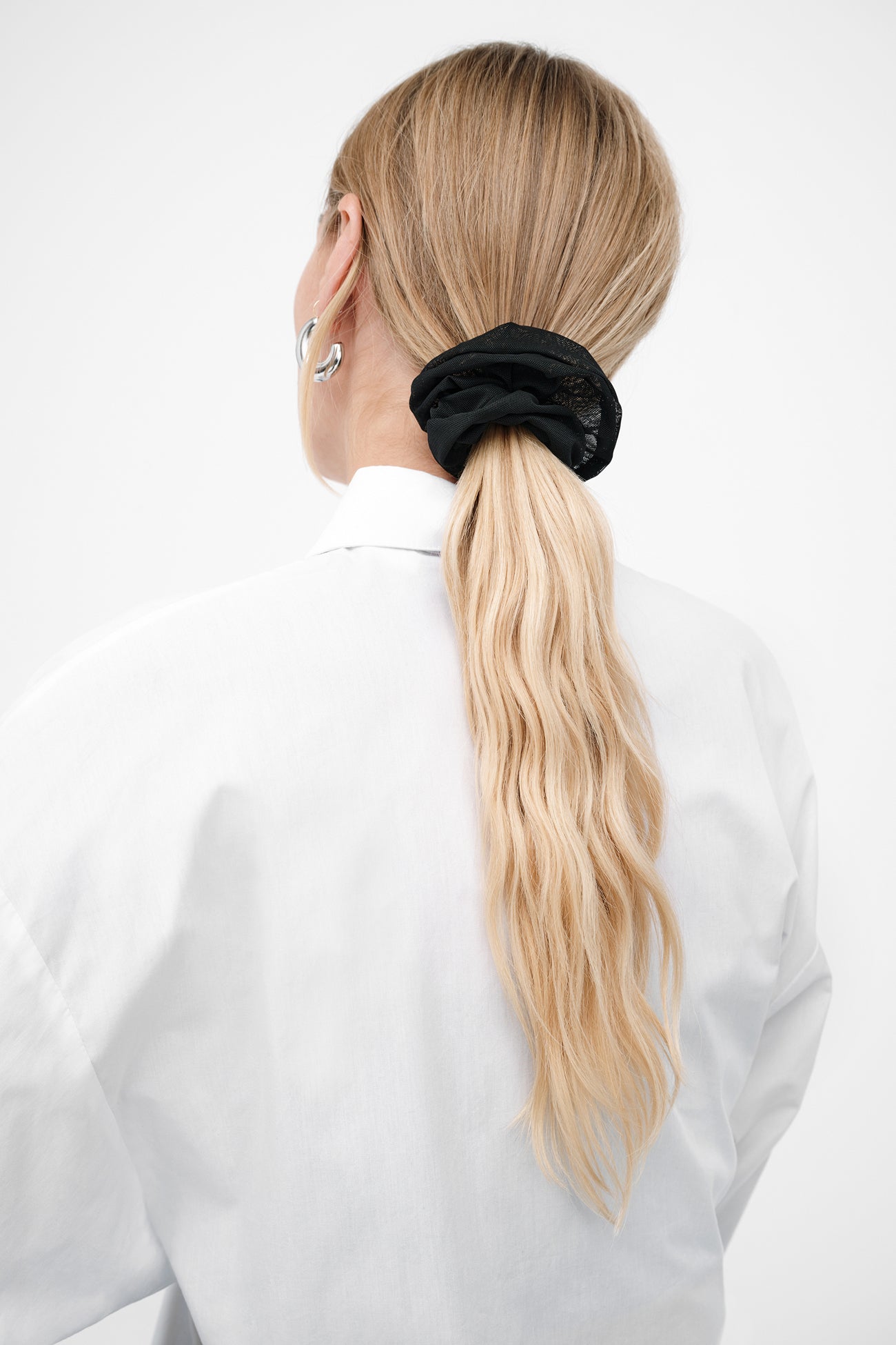 Black textured scrunchie holding a blonde ponytail on a person wearing a white shirt.