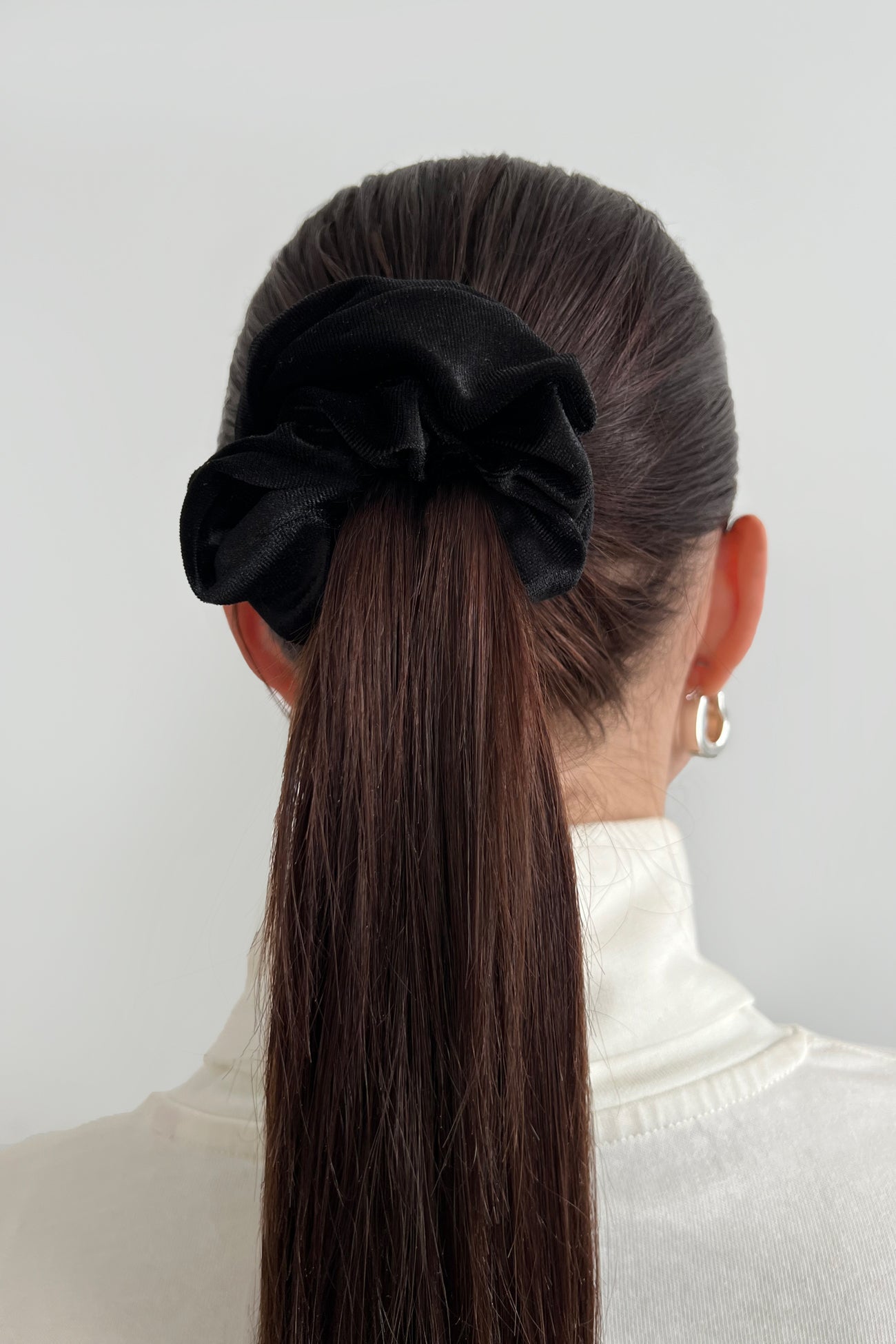 Black velvet scrunchie with bow detail worn in long brown hair in a ponytail.