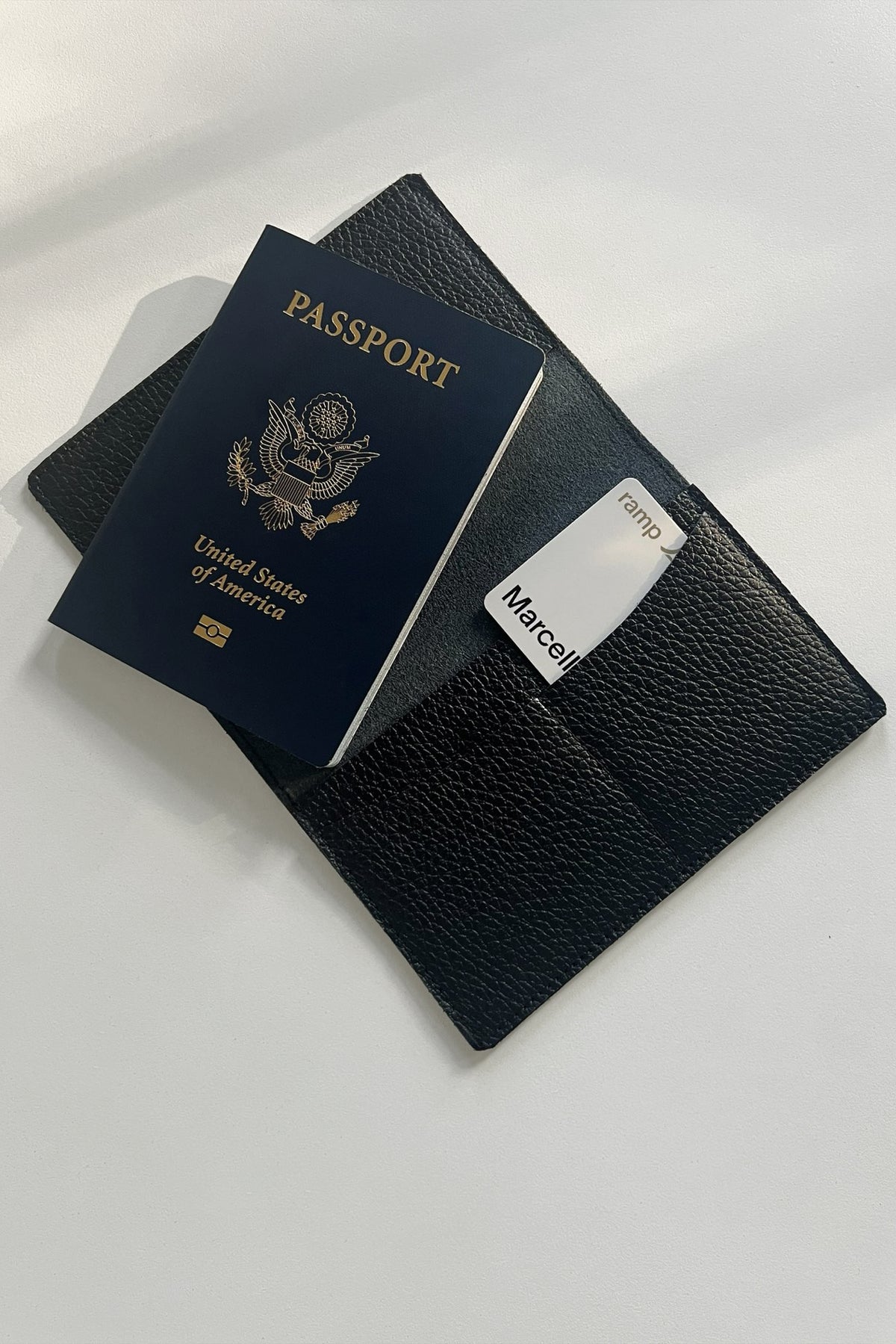 Black textured passport cover with white name label holding a blue US passport.