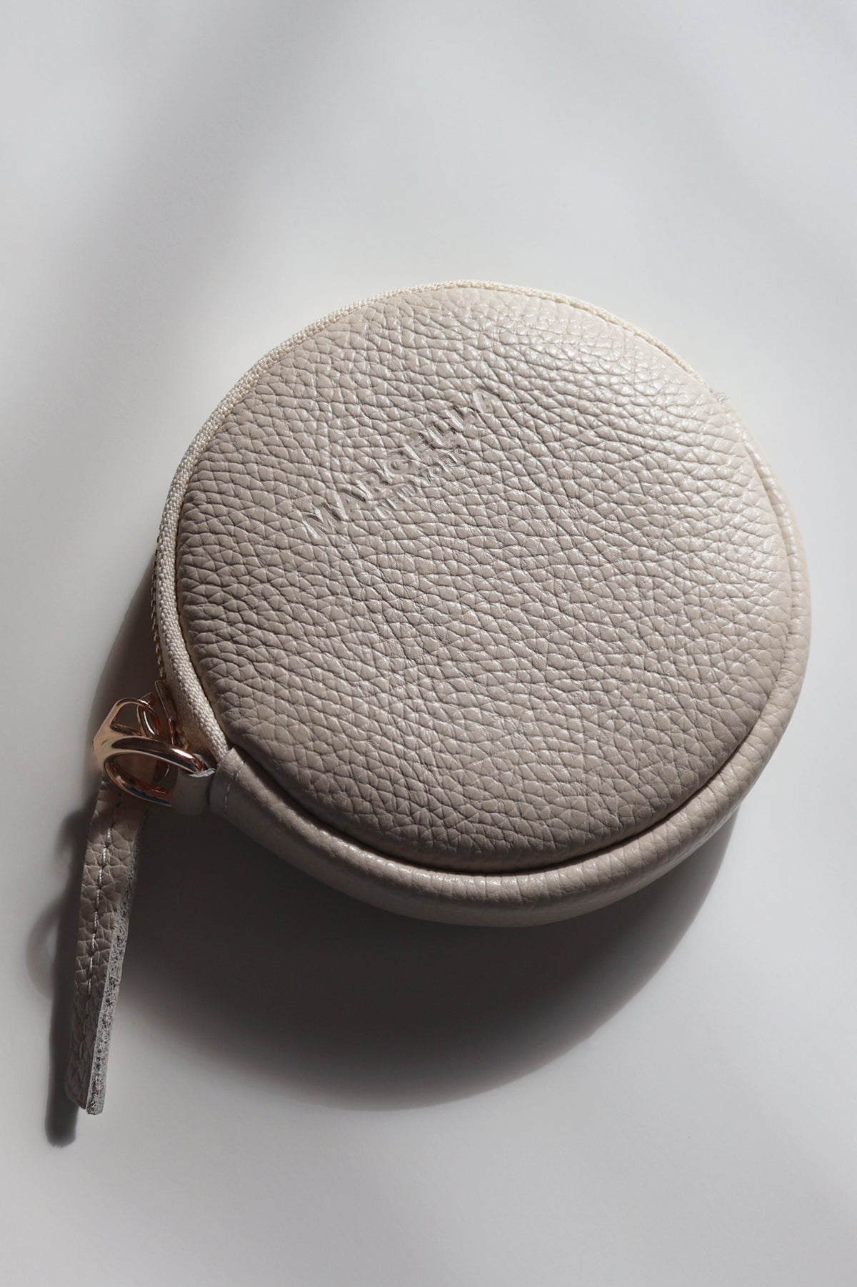 Cream leather circular pouch with textured surface and rose gold zipper pull.