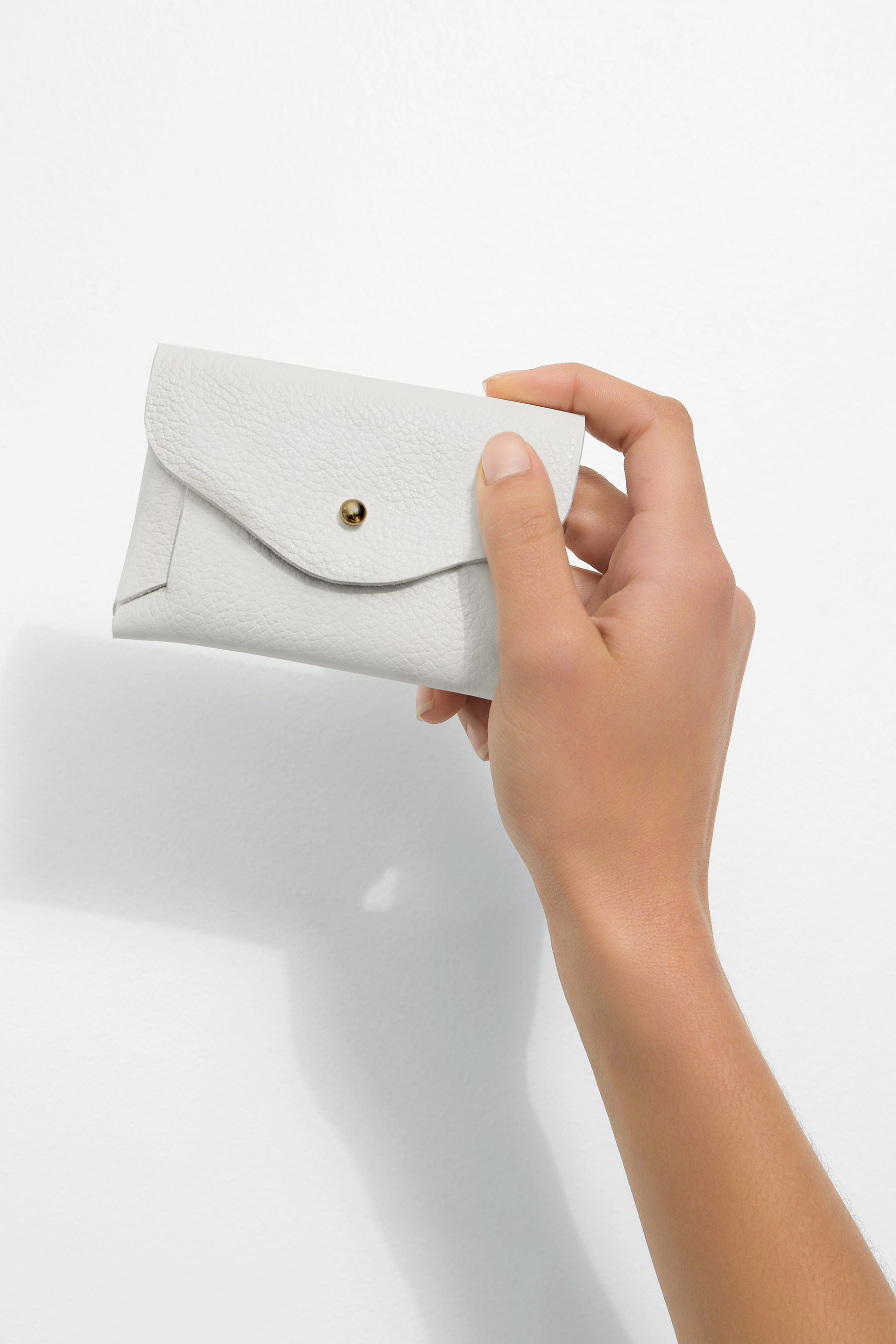 White textured leather pouch with envelope flap closure and gold snap button, held in hand.