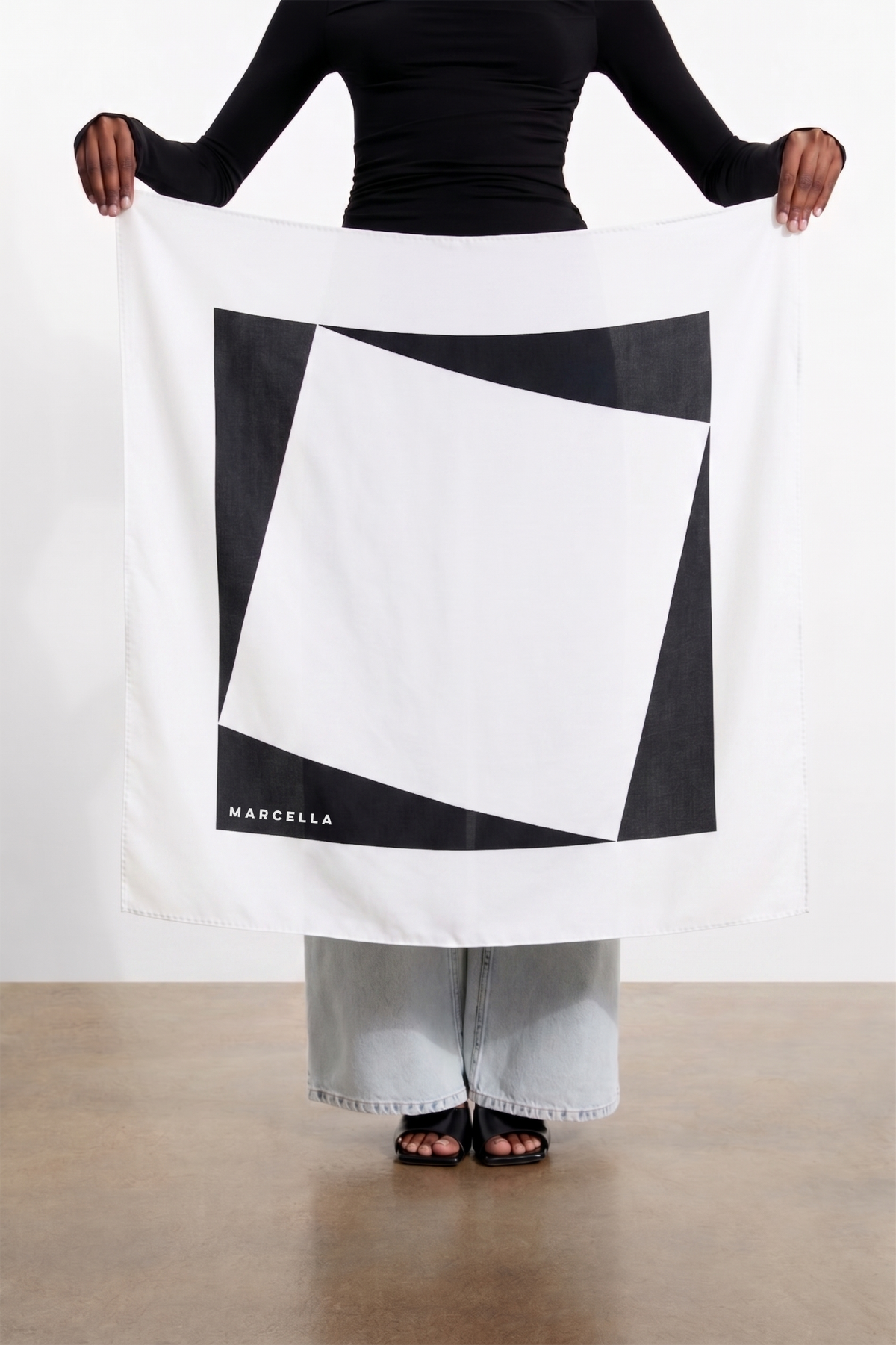 White scarf with black and white geometric design held open by person wearing black long-sleeve top.