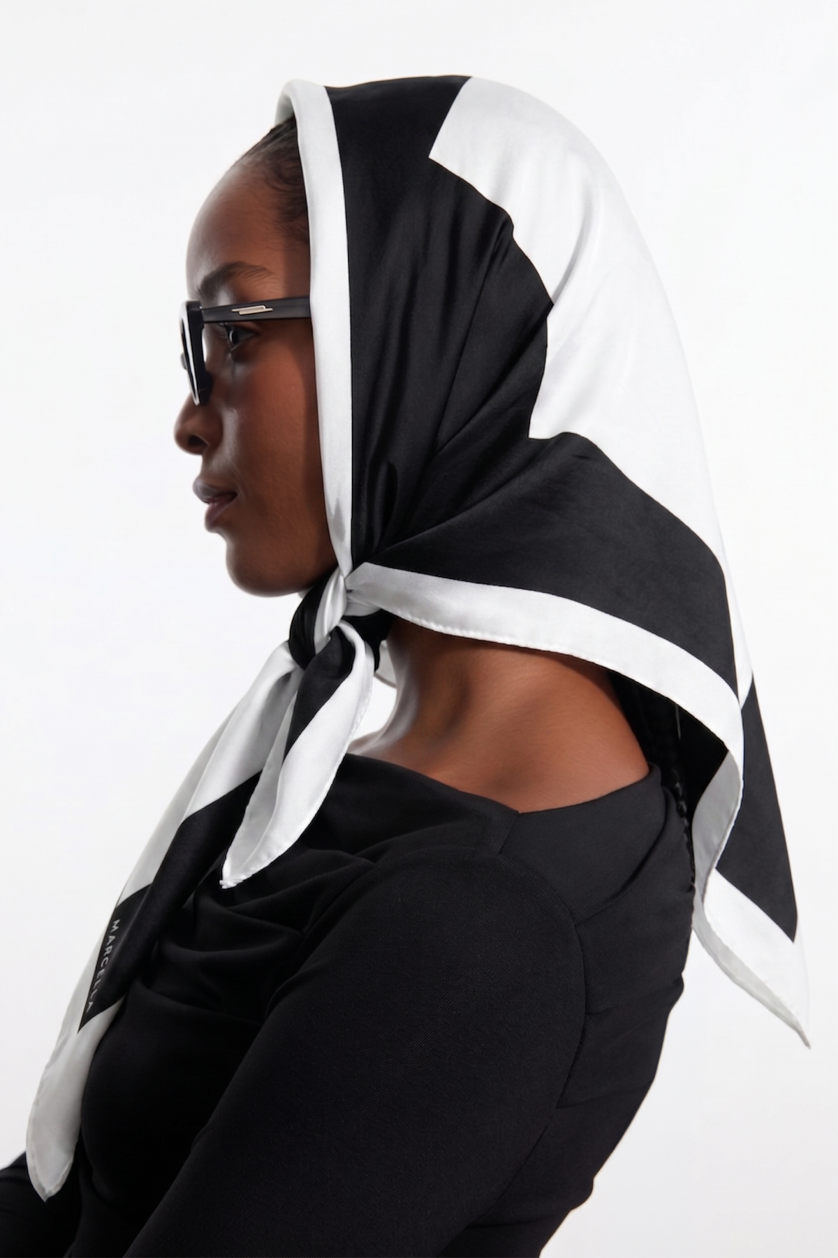Black and white color-block scarf tied around woman's head and shoulders in head wrap style.