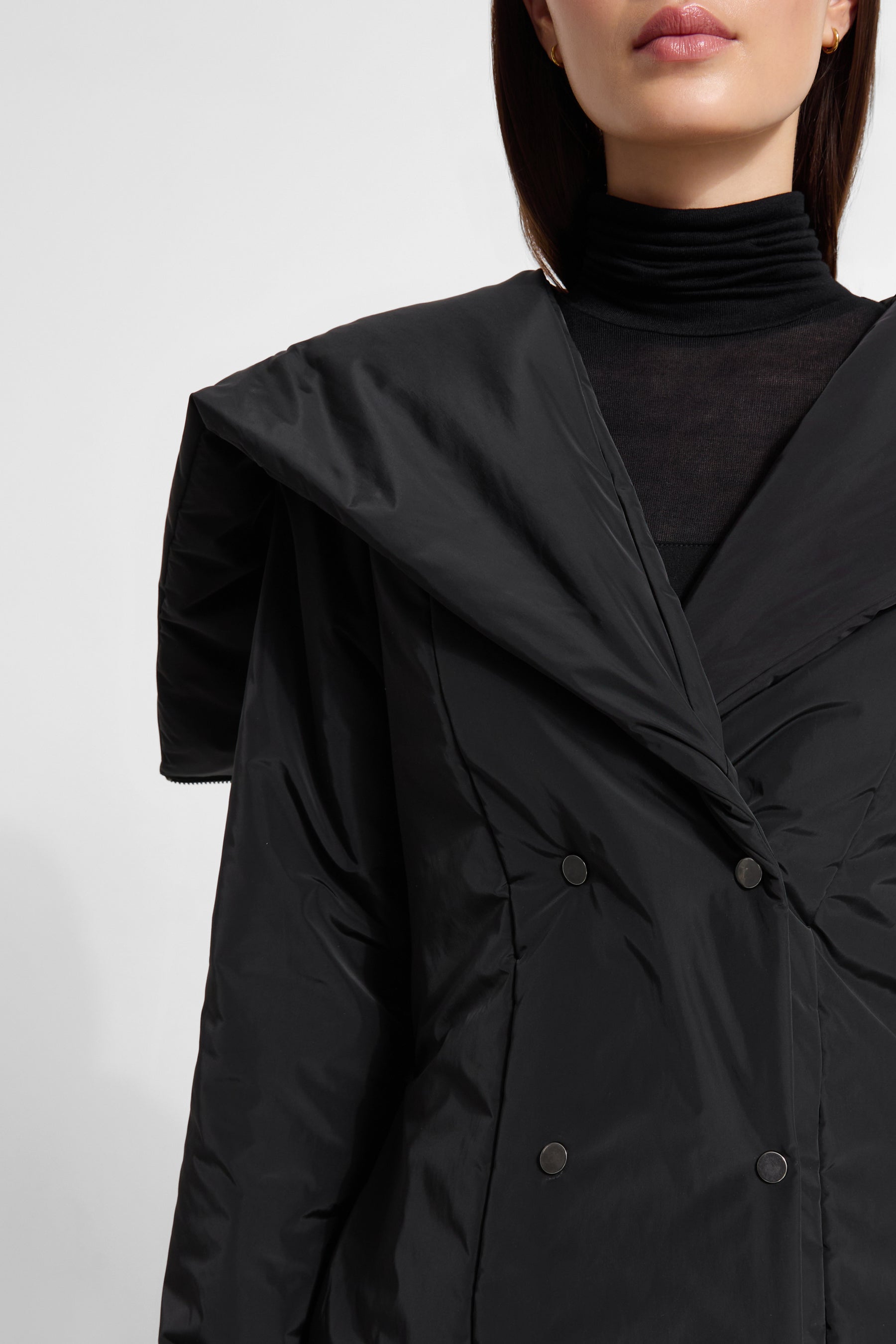 Black hooded puffer jacket with double-breasted buttons and oversized collar worn over turtleneck.