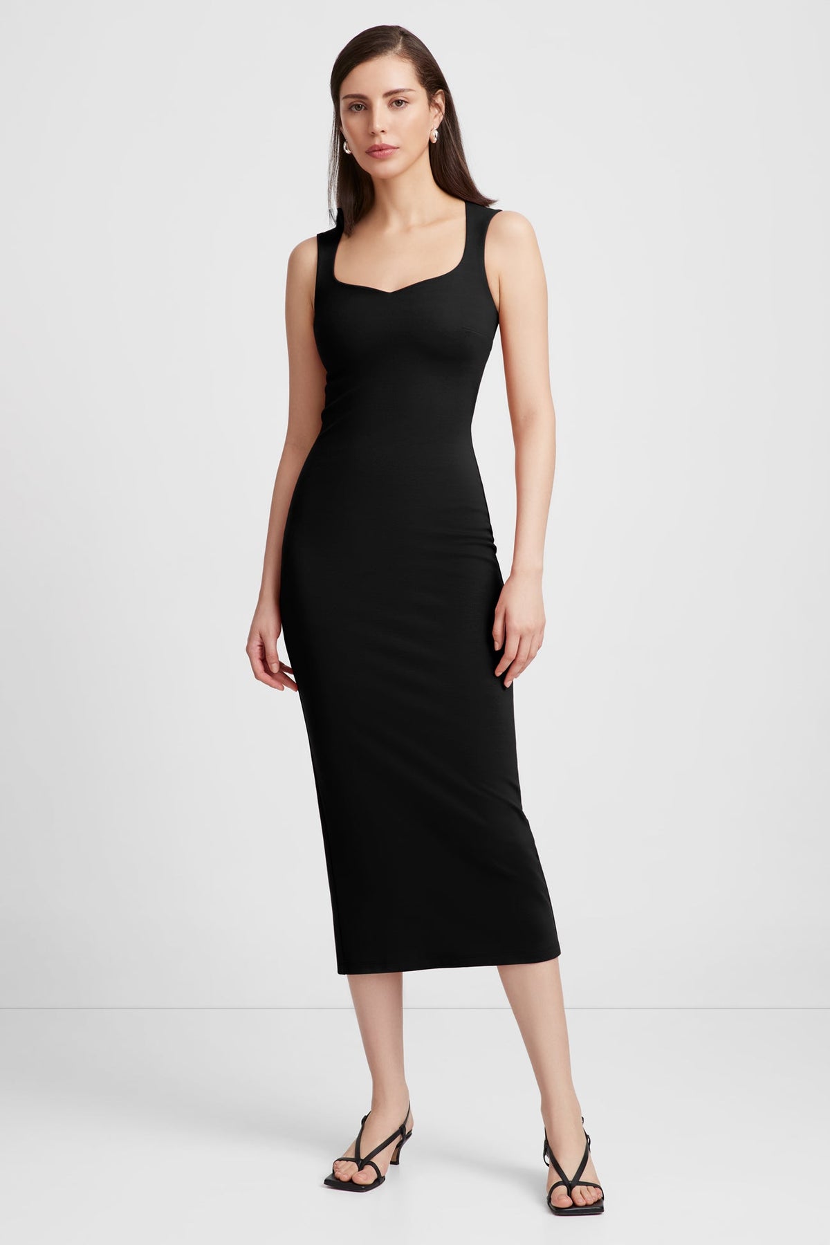 Black sleeveless midi dress with sweetheart neckline on model wearing strappy black sandals.