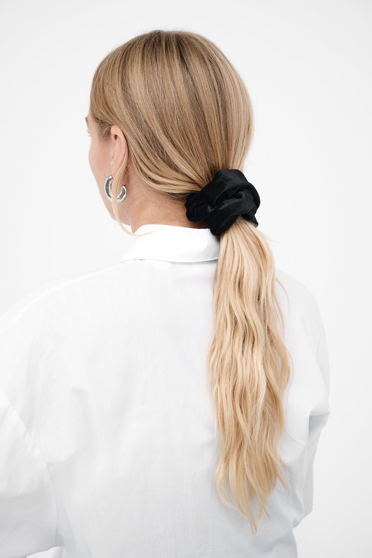 Black velvet scrunchie holding a blonde ponytail on a person wearing a white shirt.