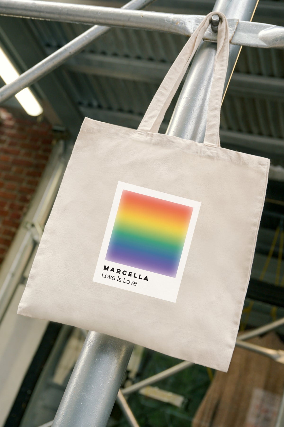 Natural canvas tote bag with rainbow gradient square print and "Marcella Love Is Love" text.