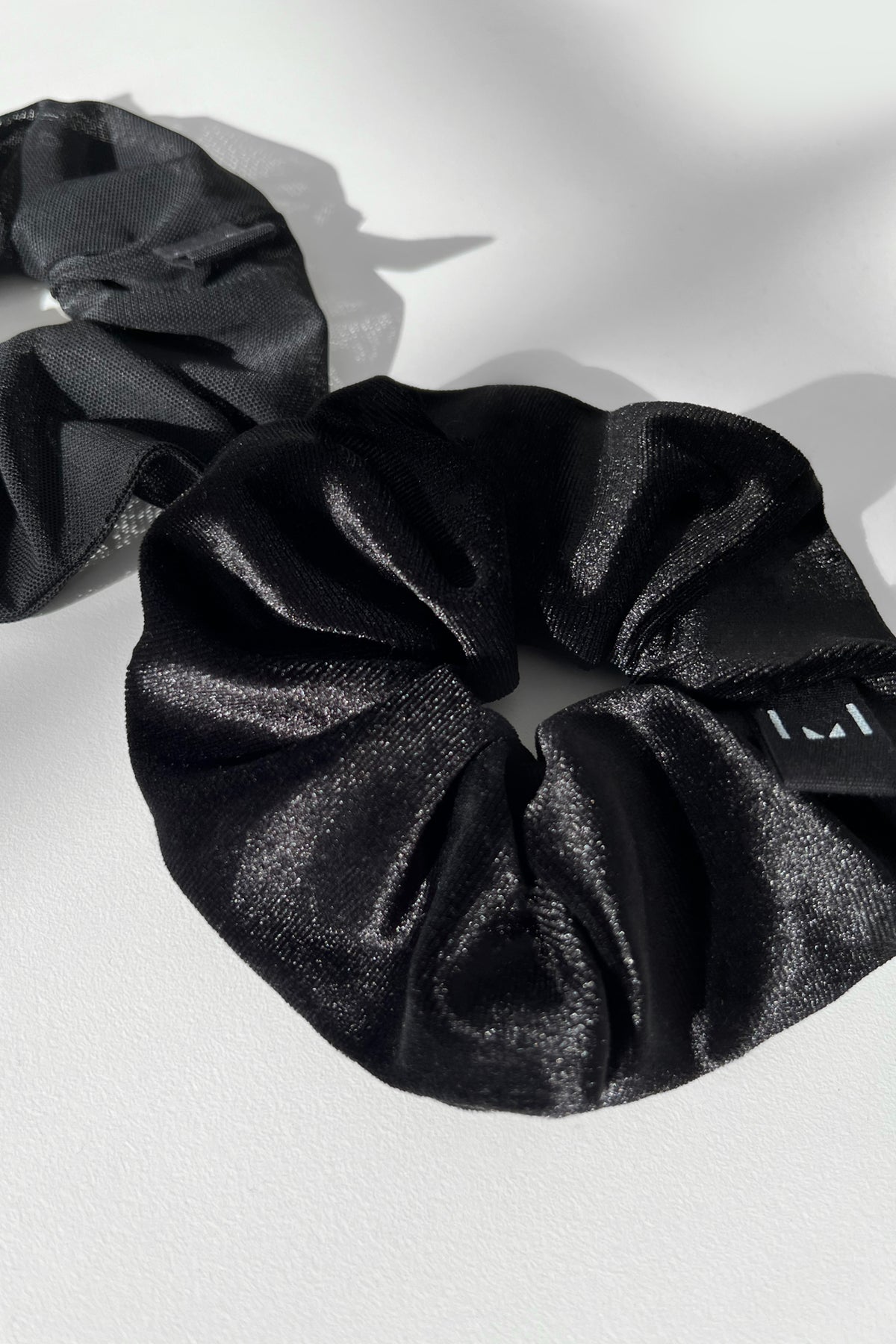 Three fabric scrunchies in black and gray with metallic sheen detail.