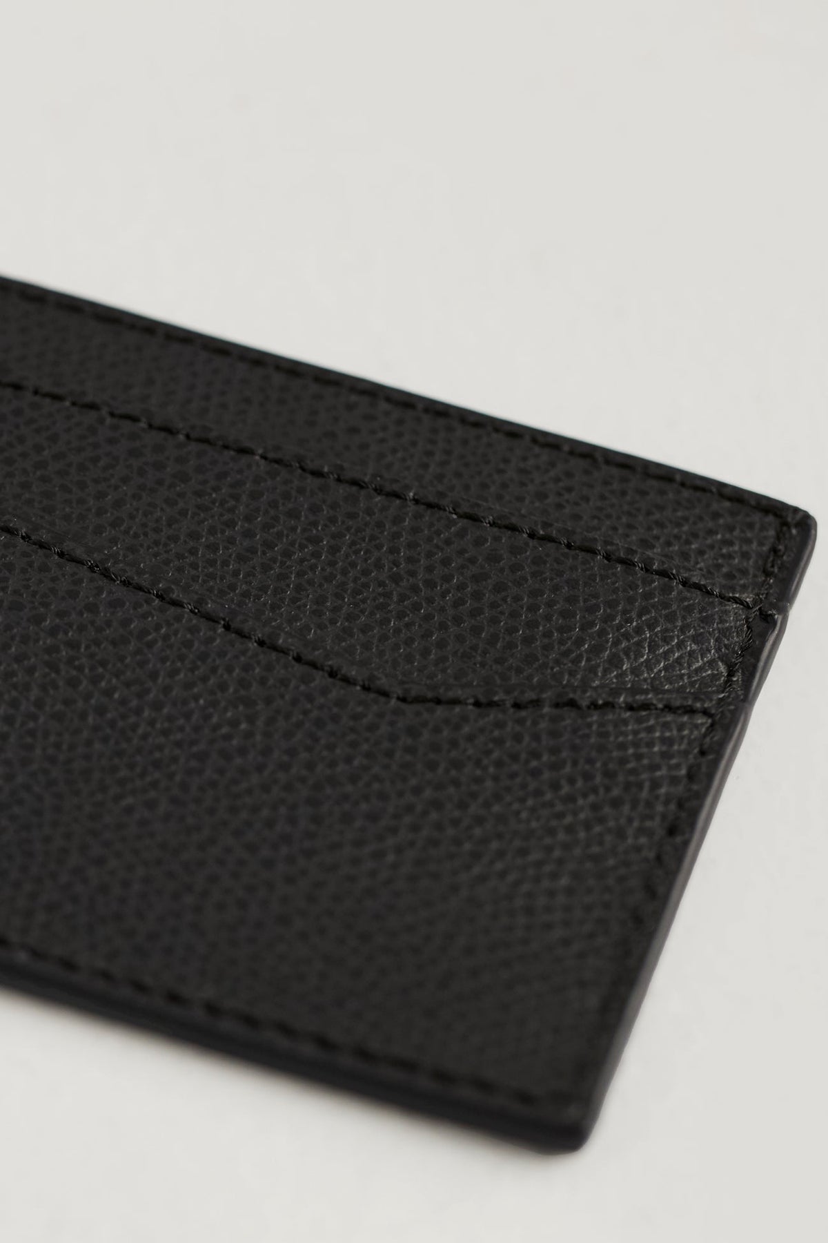 Black leather card holder with curved card slots and stitched seams on a white background.