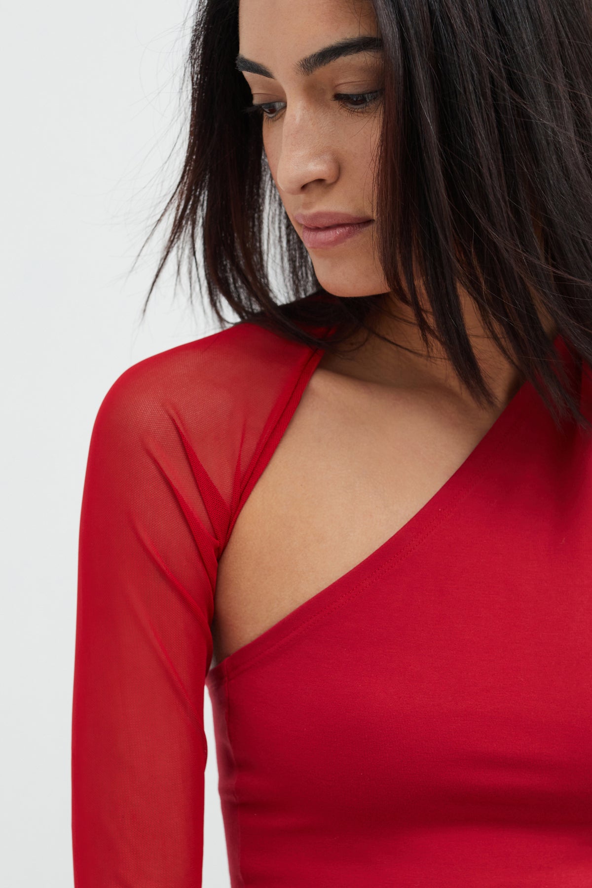 Red wrap top with sheer mesh sleeves worn by model looking downward.
